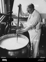 man-in-white-coveralls-using-a-large-ladle-to-stir-a-pot-of-milk-in-K1DAT9.jpg